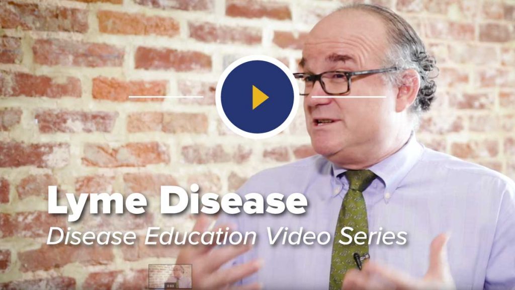 Dr John Aucott sitting in a chair in front of a brick wall discussing Lyme Disease